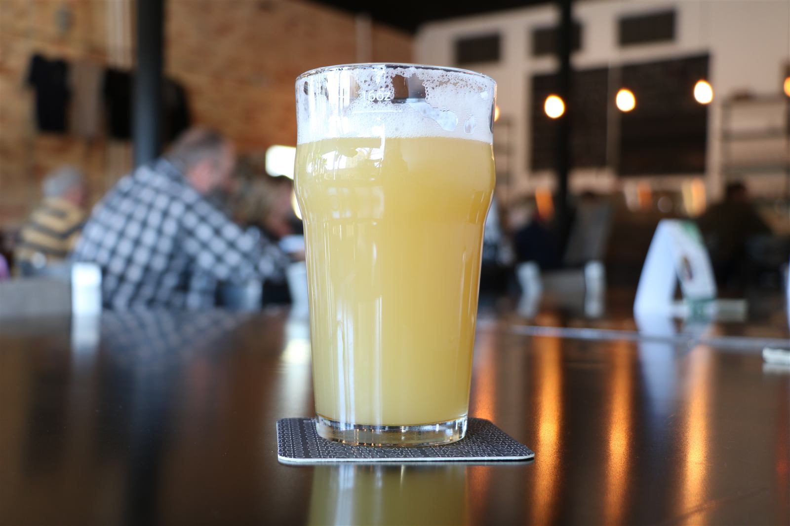 A hazy pint on the bar with the taproom and its regulars behind it
